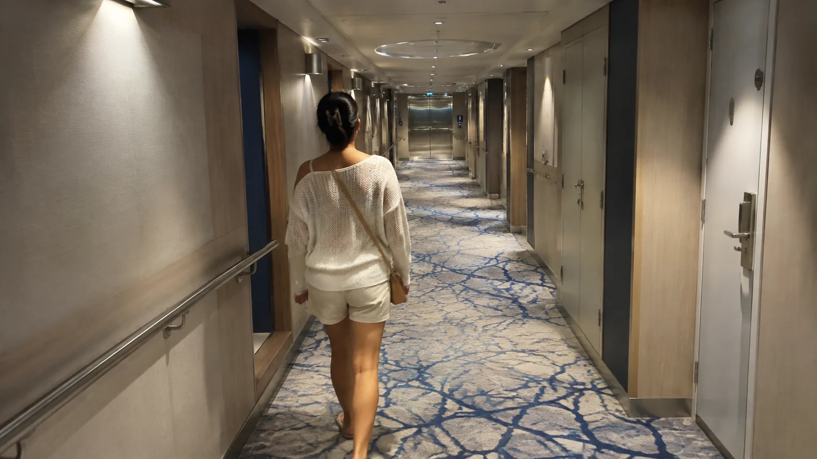 Woman walking down a long carpeted corridor lined with cabin doors.