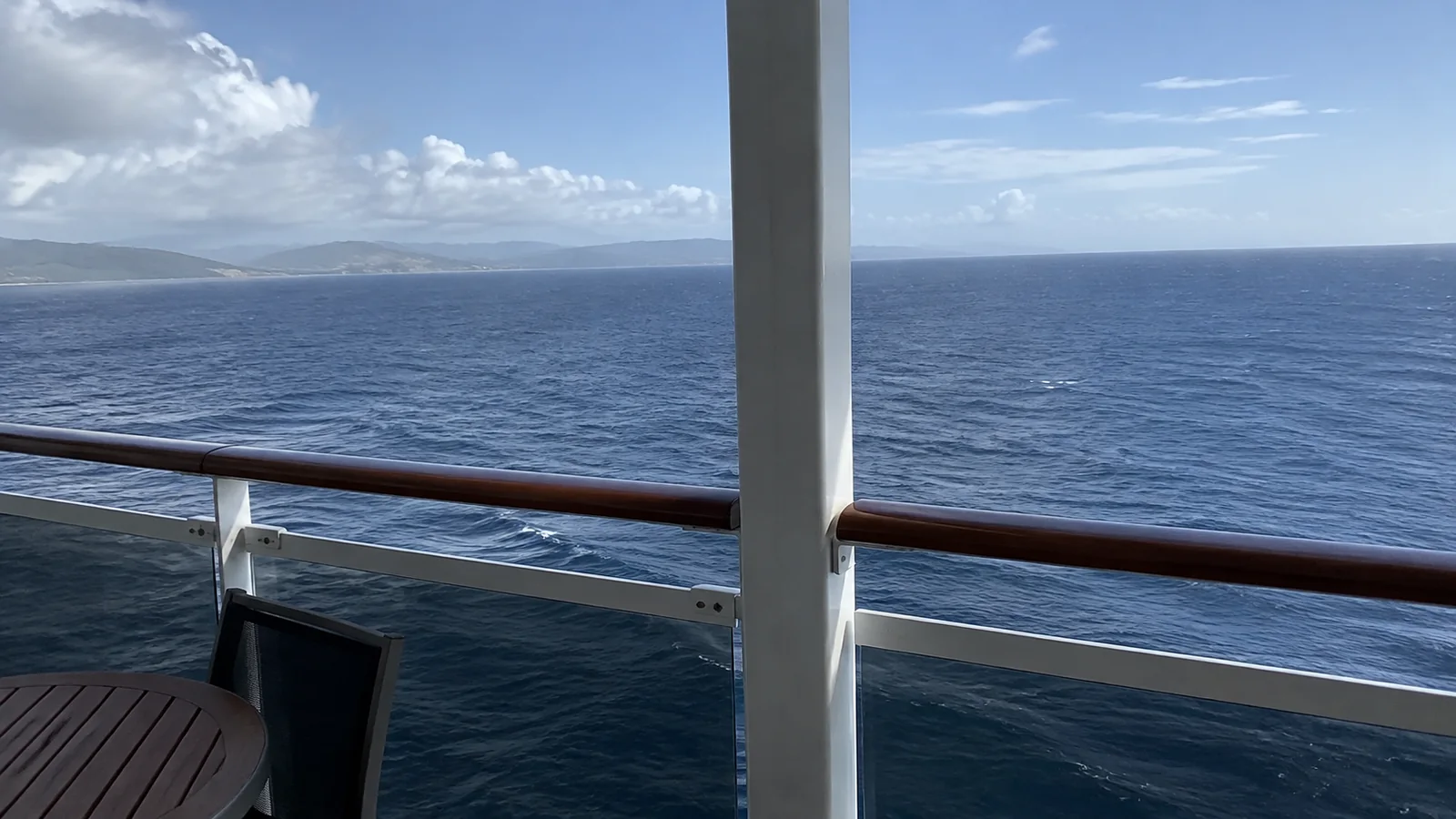 Ocean view from a ship balcony with a railing and dark chair.