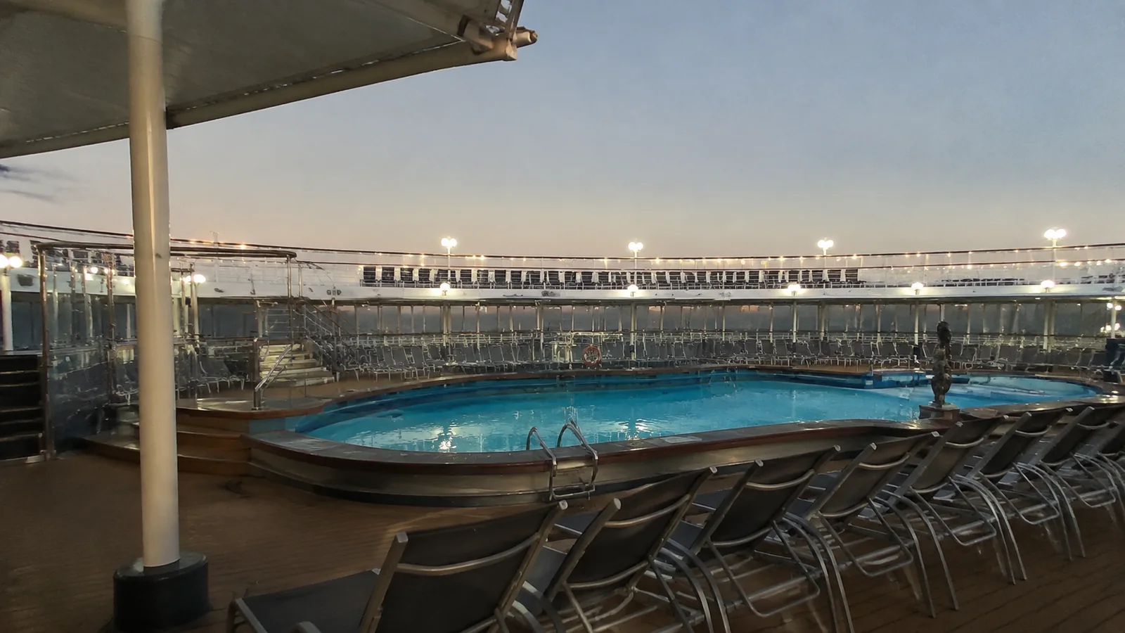 Empty loungers surrounding an outdoor ship pool at dusk.