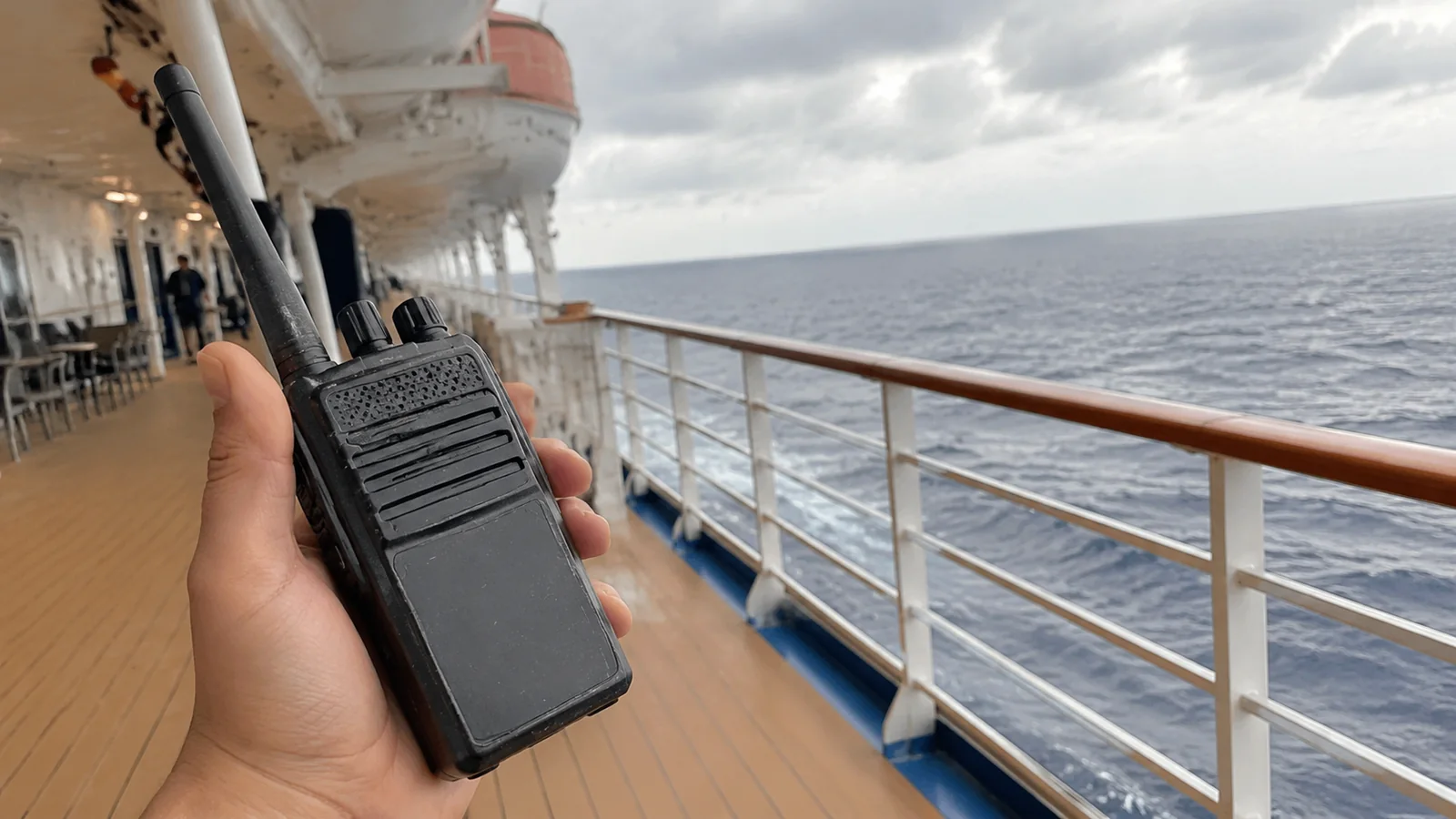 Hand holding a walkie-talkie on an open cruise ship promenade