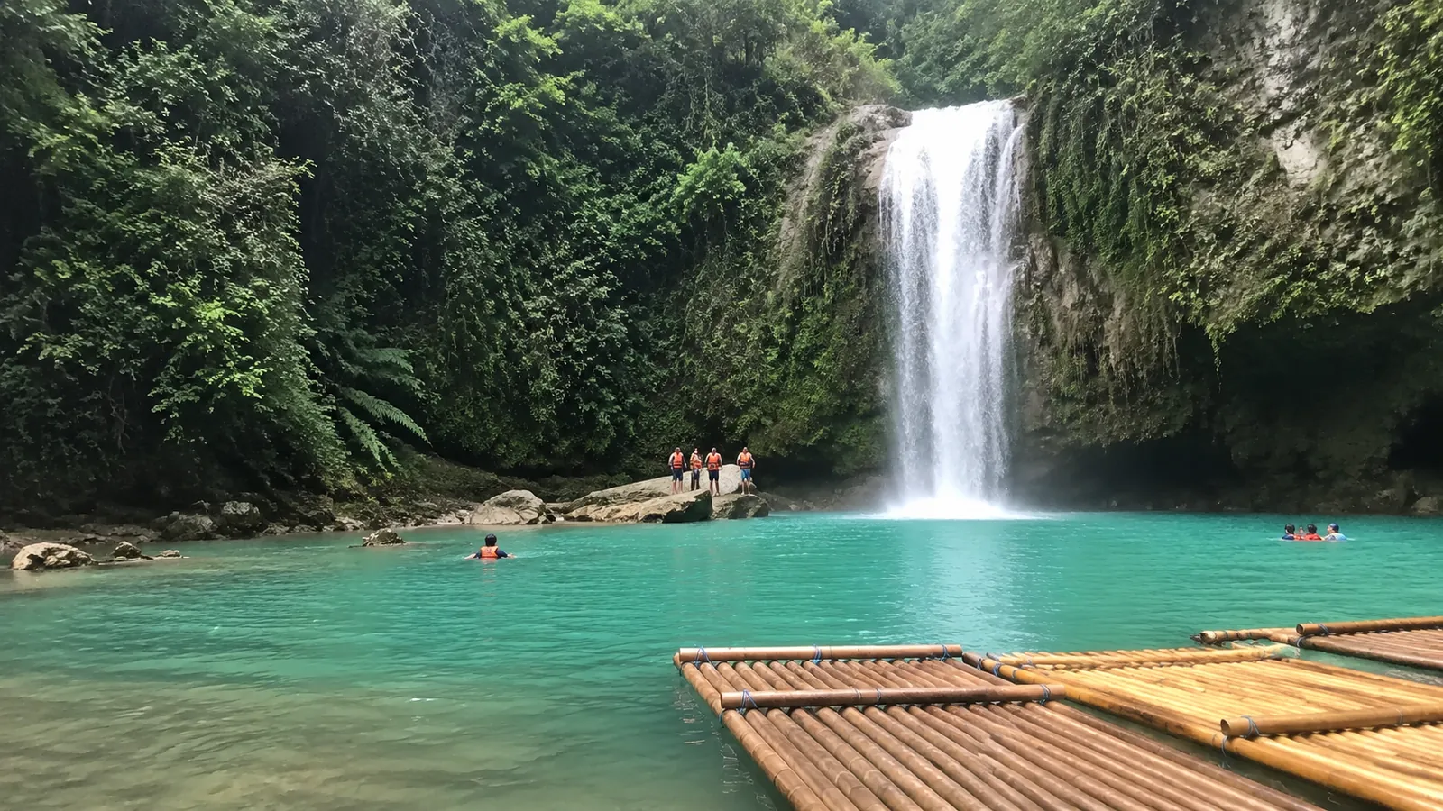 Turquoise waterfall pool with bamboo rafts along the shore