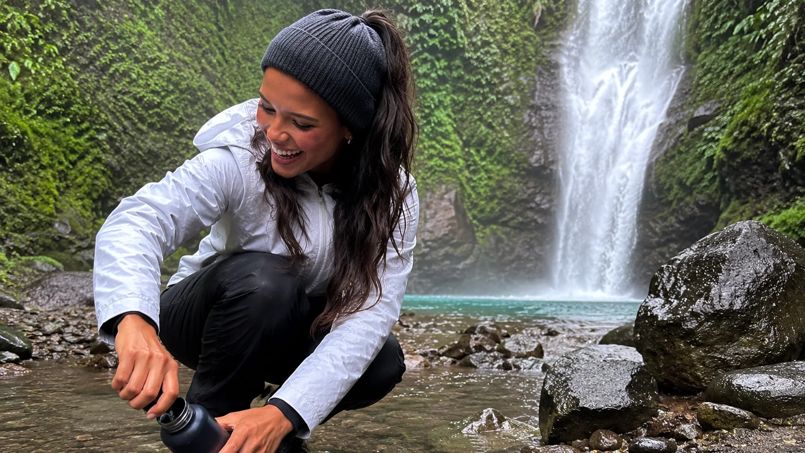 Woman crouching on rocks with a waterfall behind her