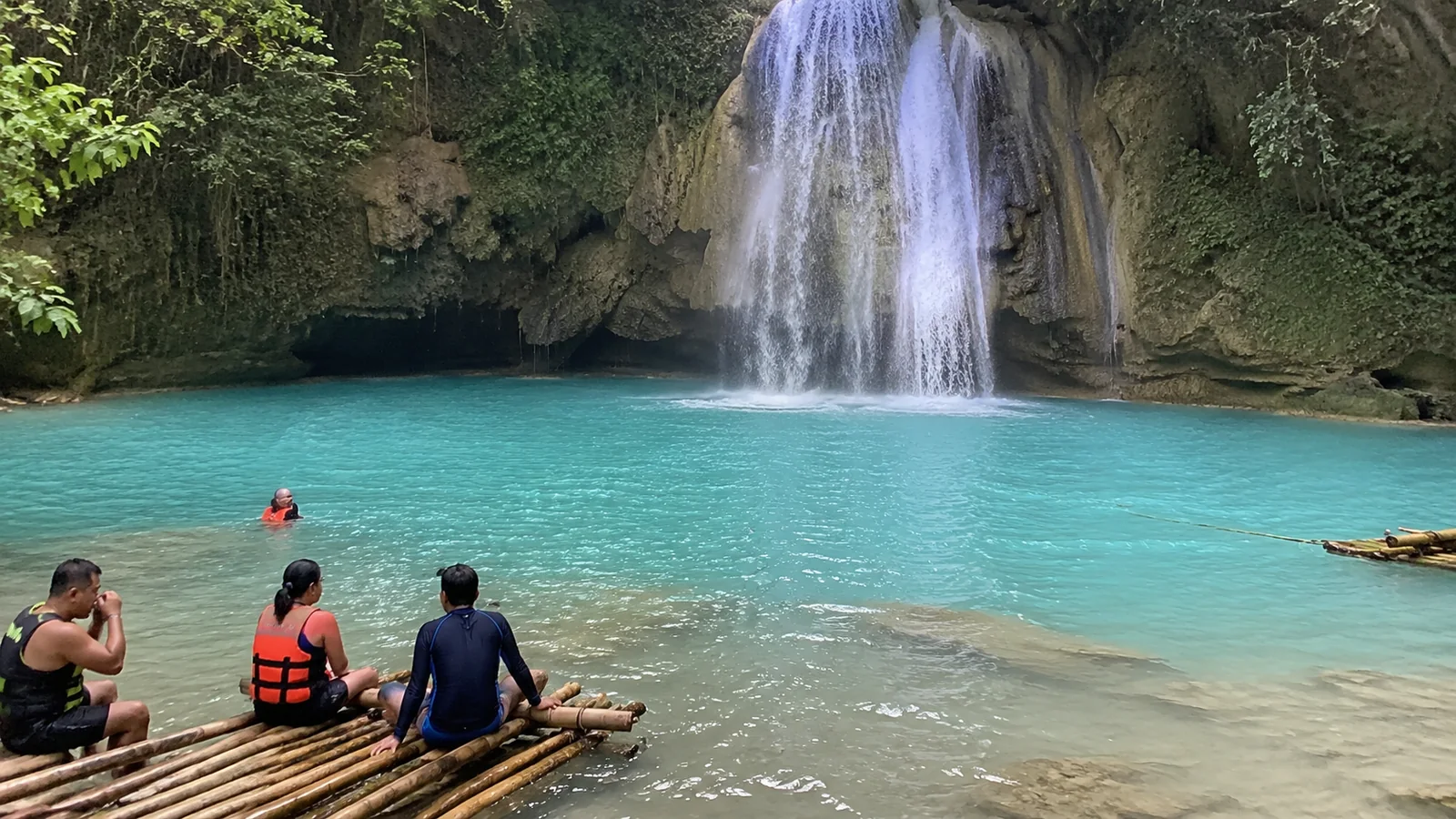Visitors seated on a bamboo raft facing a waterfall