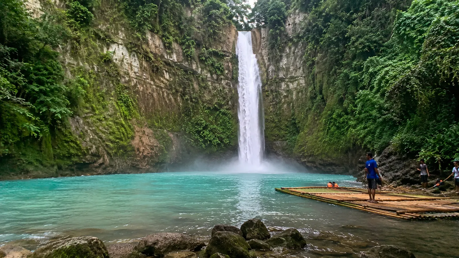 Waterfall flowing into a turquoise pool beside a bamboo raft