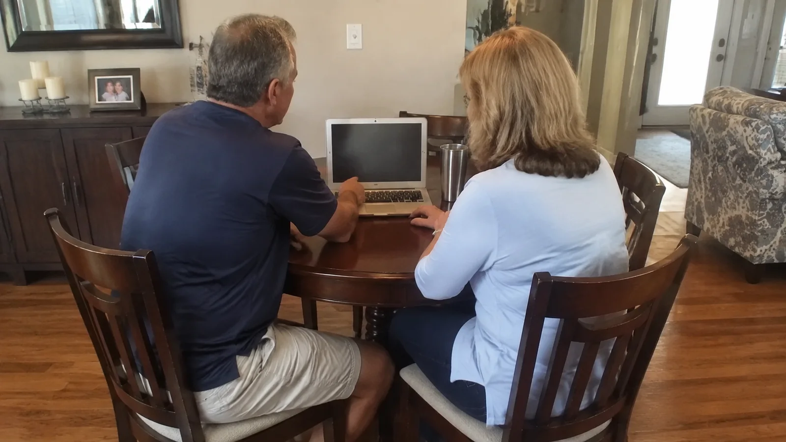 Couple sits at a dining table looking at a laptop.