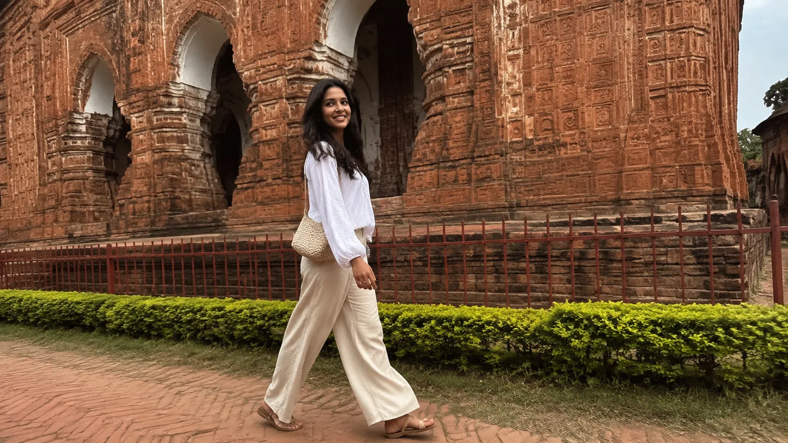 Woman walks beside an ornate red terracotta temple.