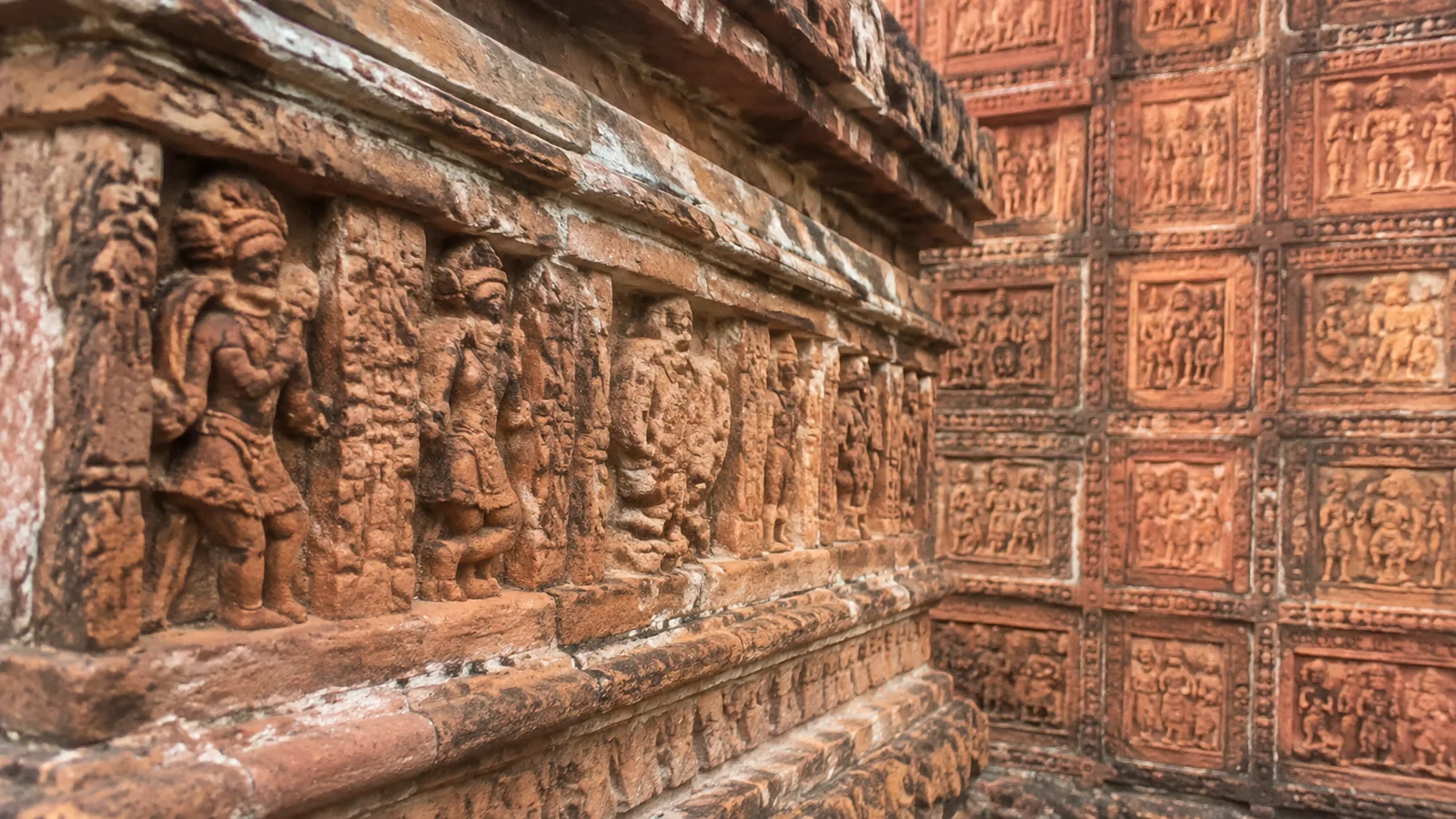 Carved figures and decorative panels cover a weathered terracotta temple wall.