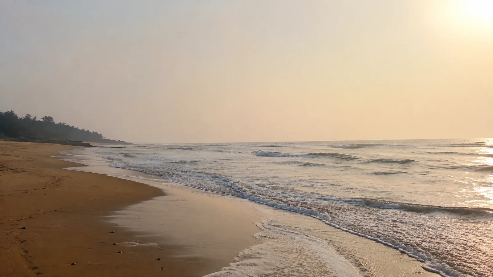 Gentle surf washes onto a sandy beach in warm evening light.