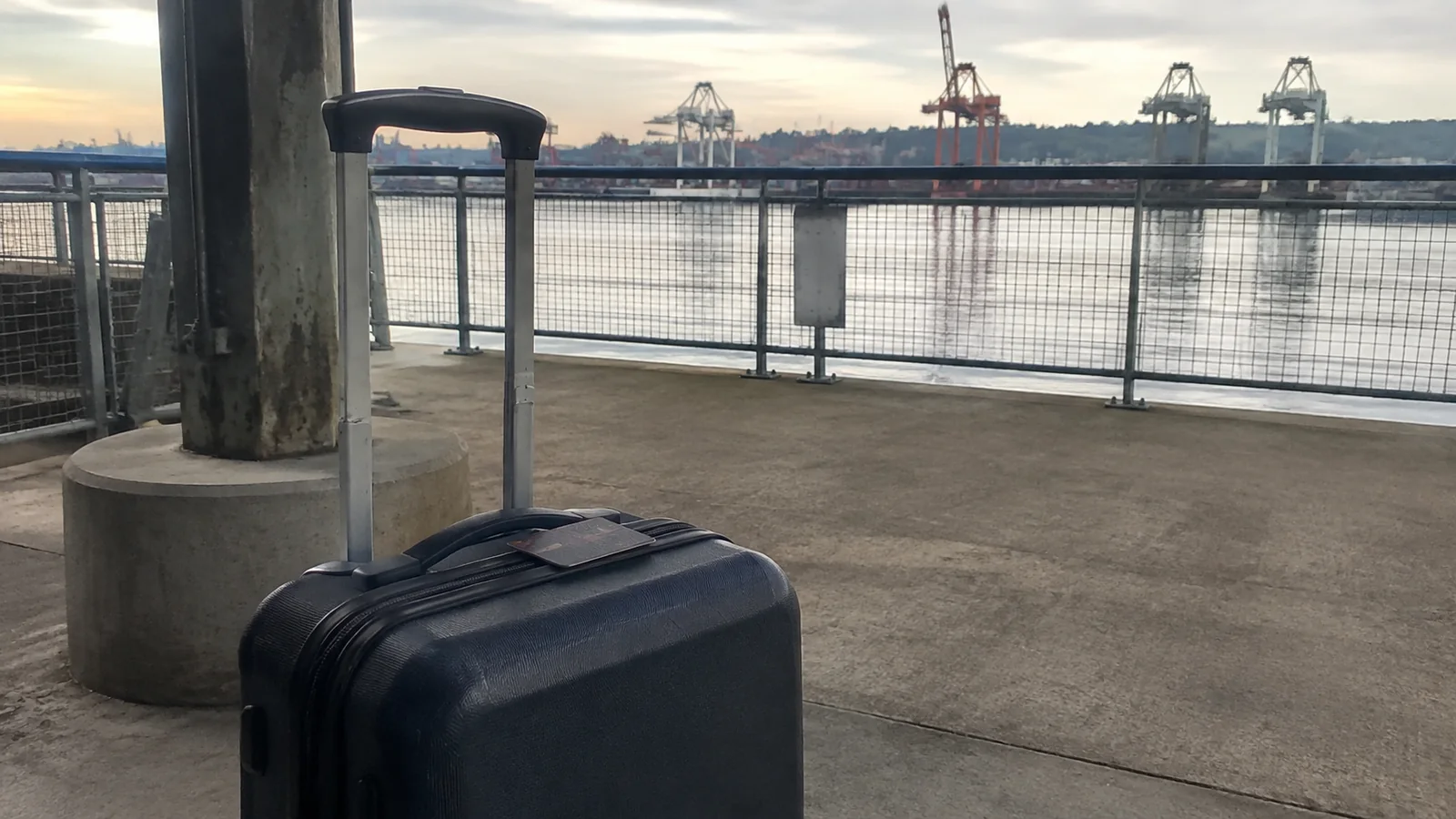 Rolling suitcase beside a waterfront terminal railing