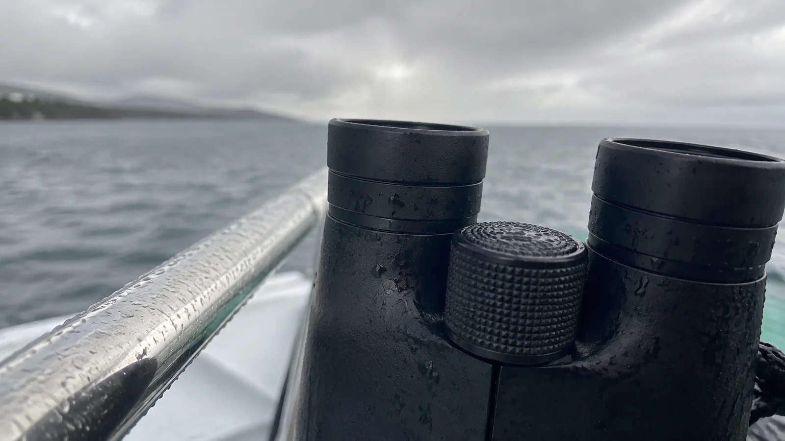 Binoculars resting beside a boat railing above gray water