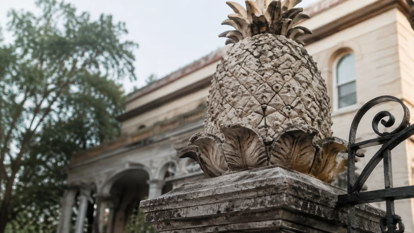 Carved stone pineapple on a gatepost beside an iron fence.
