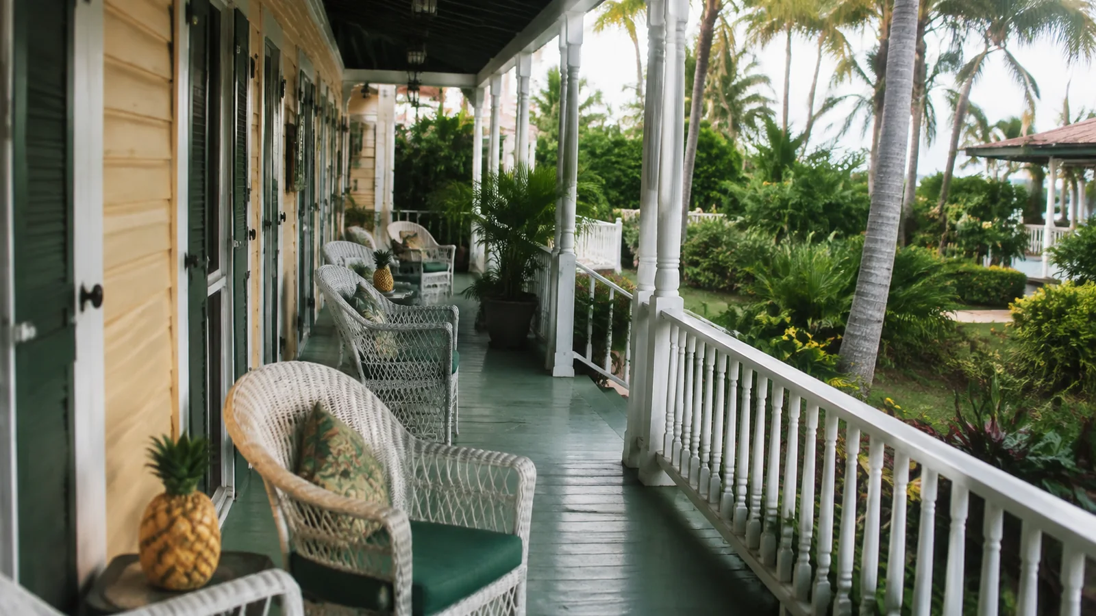 Tropical veranda with wicker chairs and a pineapple on a small table.