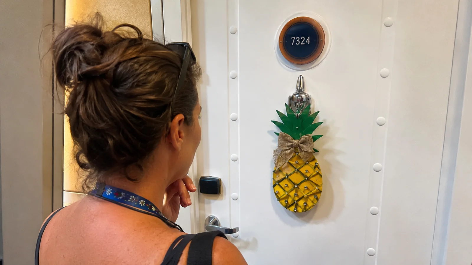 Woman looking at an upside-down pineapple decoration hanging on a cruise cabin door