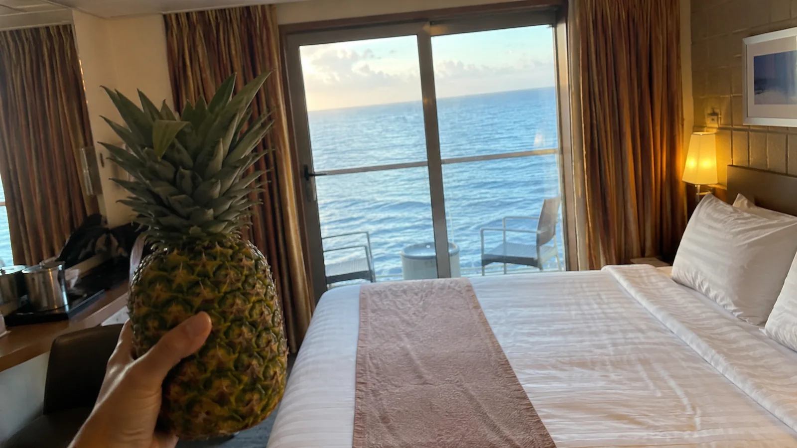Pineapple placed on a cruise cabin bed beside an ocean-view balcony