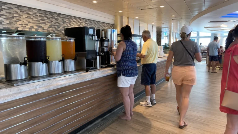 Passengers standing beside beverage dispensers in a cruise ship dining area
