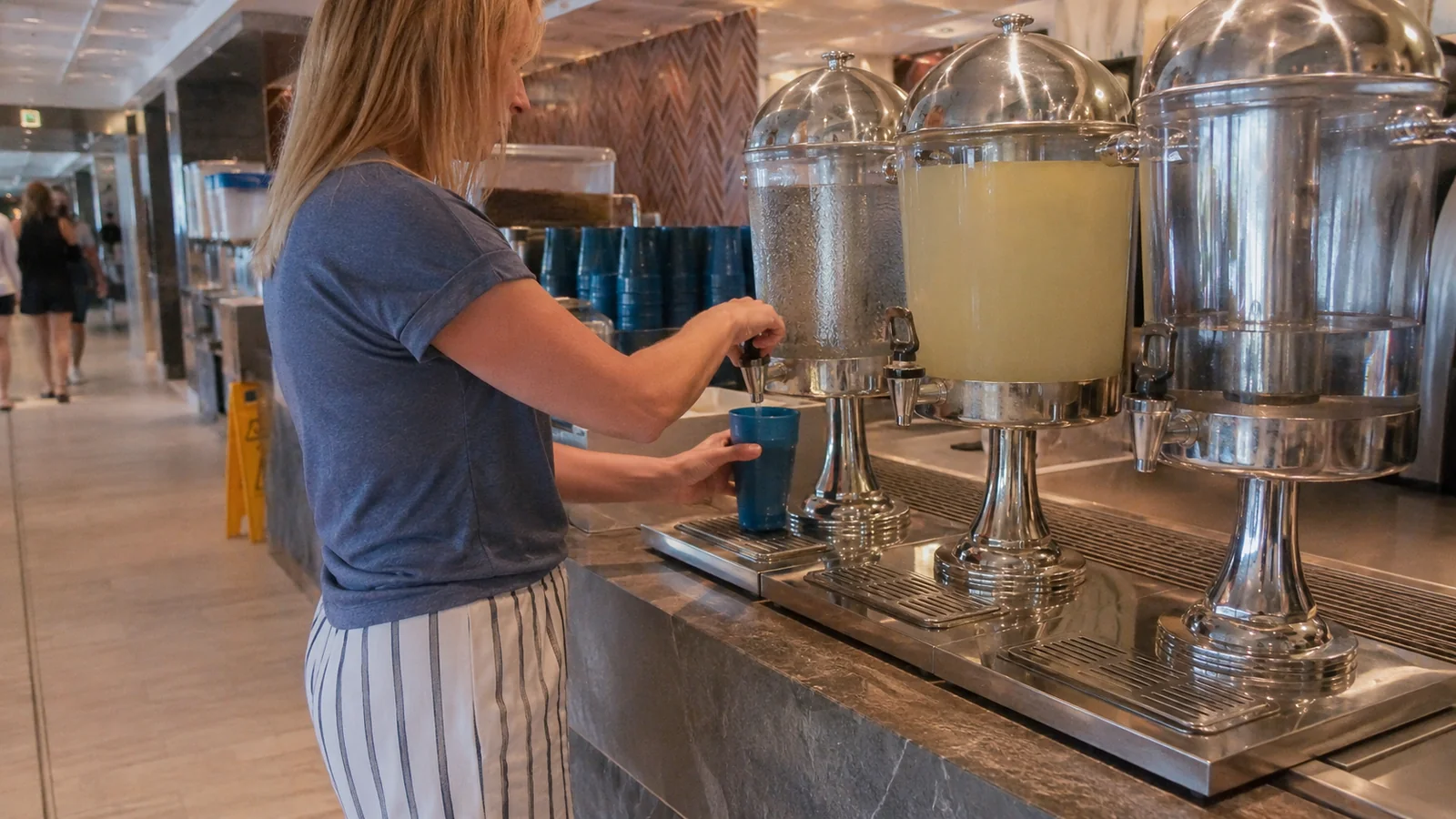 Woman filling a blue cup from large beverage dispensers on a cruise ship
