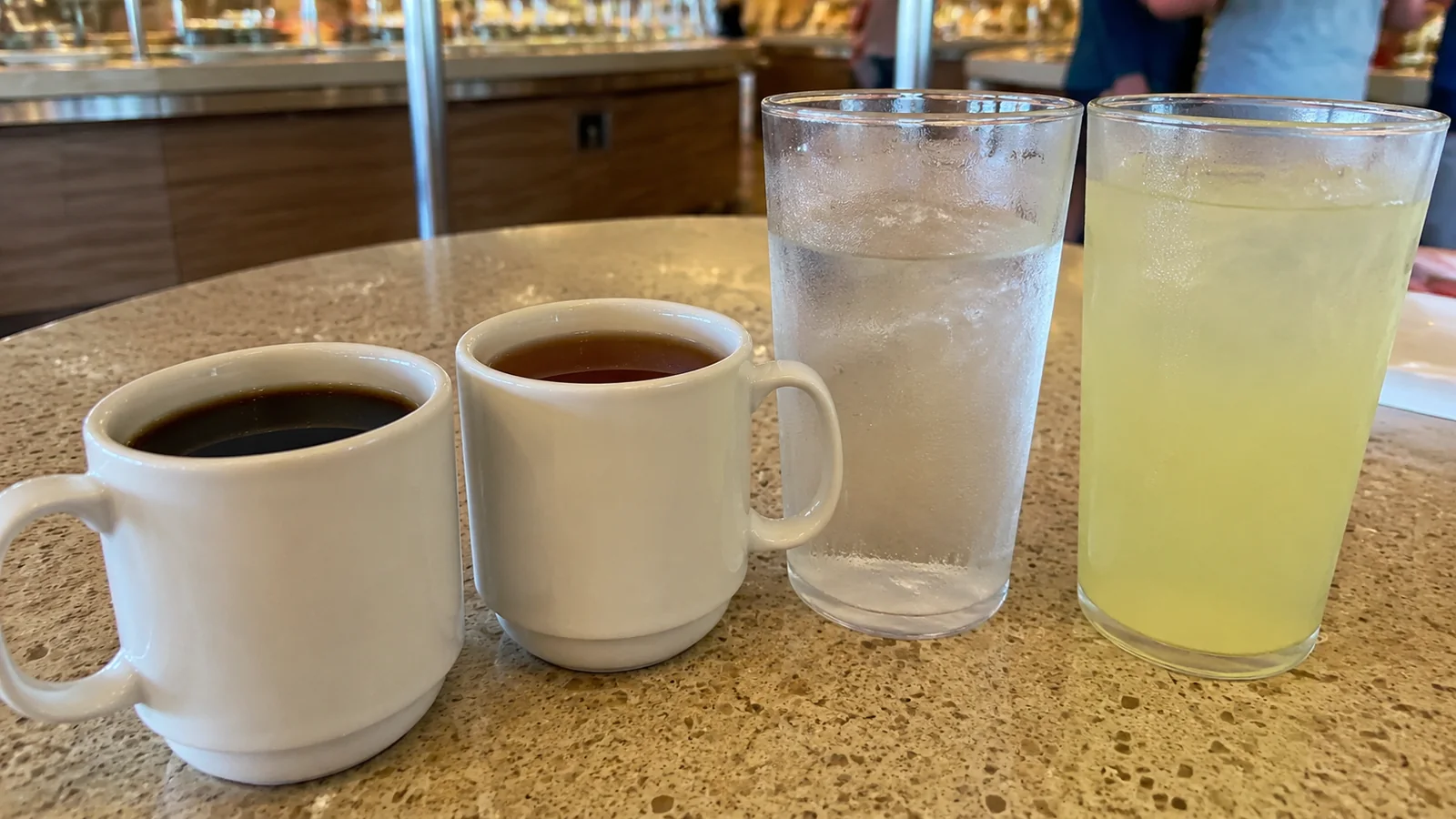 Two coffee mugs, a glass of water, and a glass of lemonade on a counter