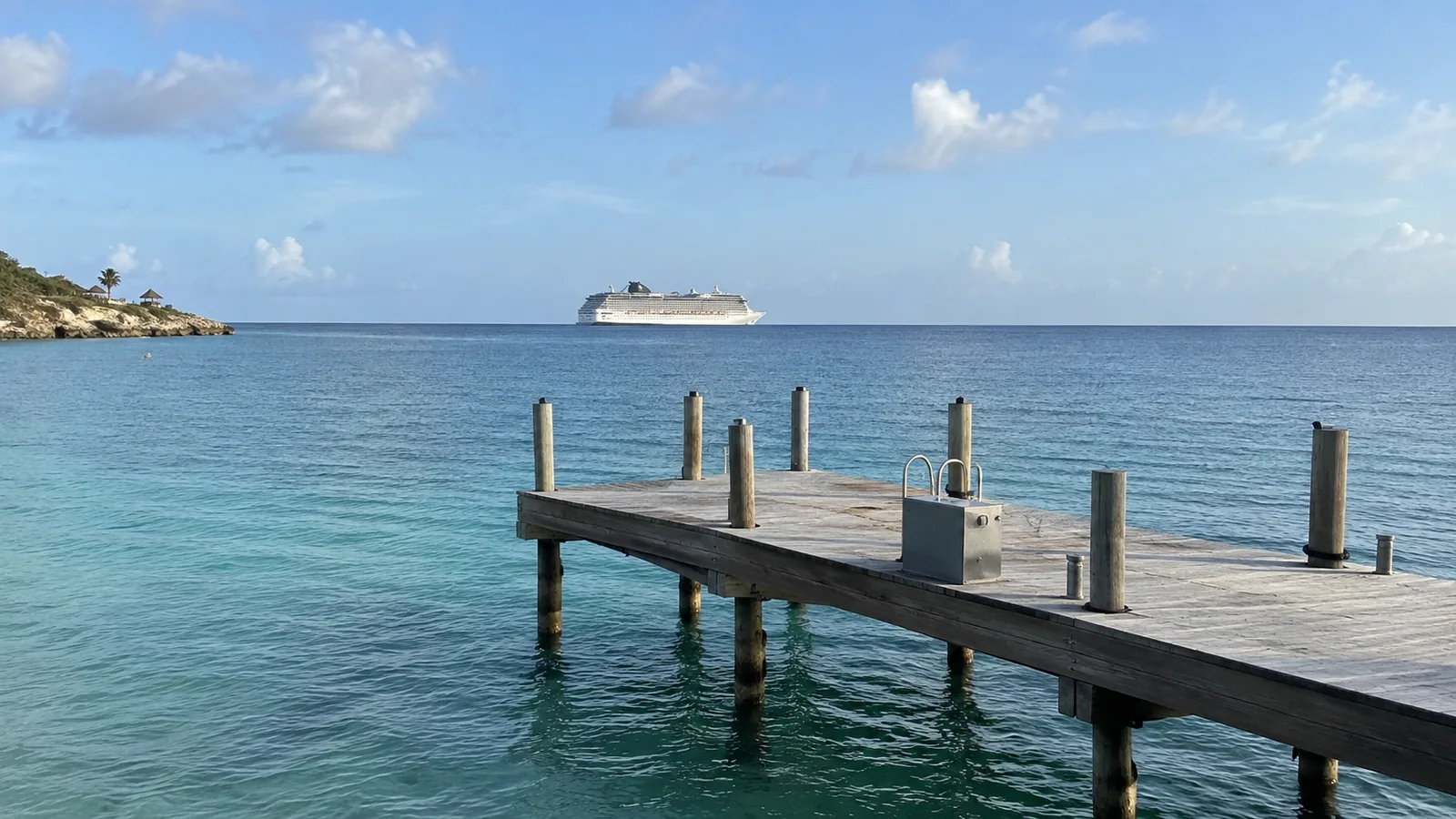 Empty wooden pier extending into clear water with a cruise ship offshore.