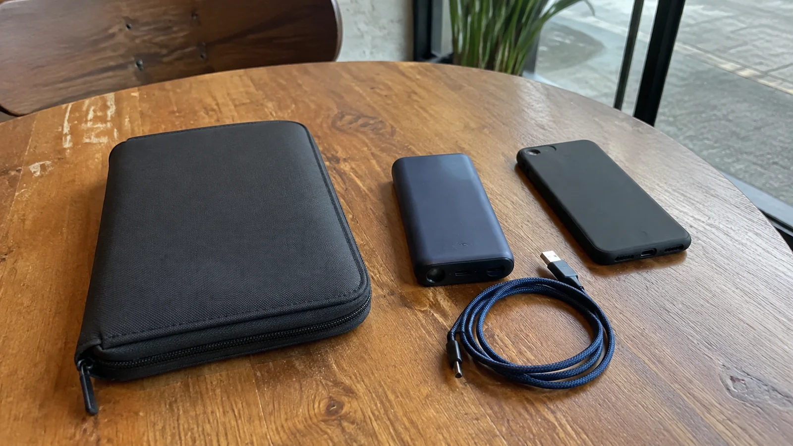Travel wallet, phone, power bank, and charging cable on a wooden table.