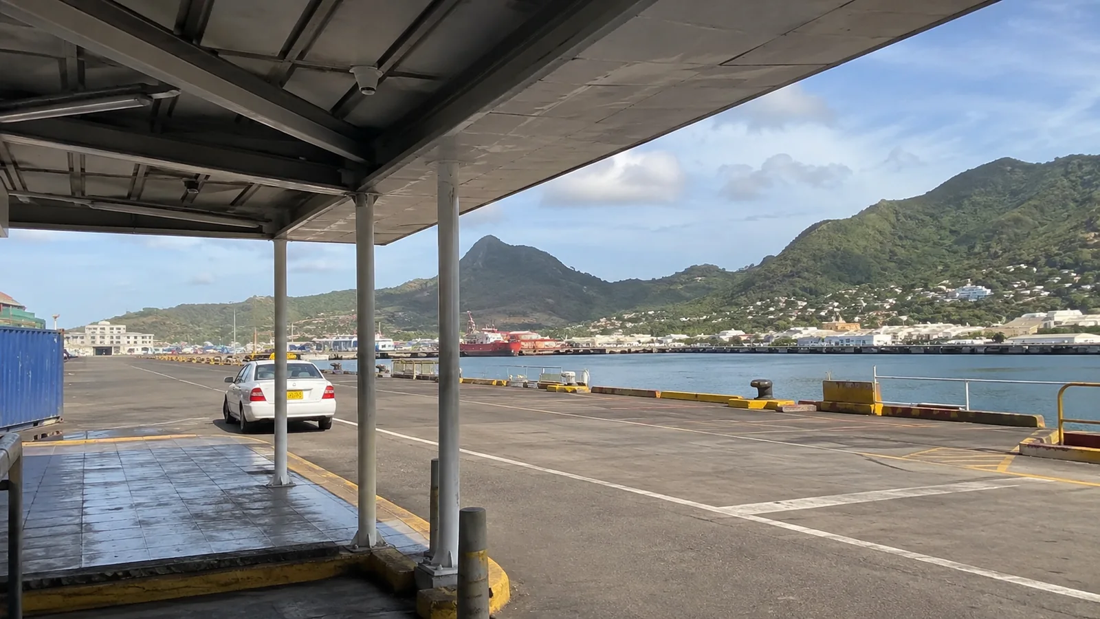 Car driving along an open pier beside a mountainous harbor.