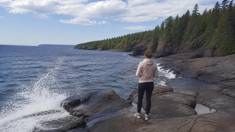 Traveler standing on shoreline rocks beside splashing lake waves and forest.