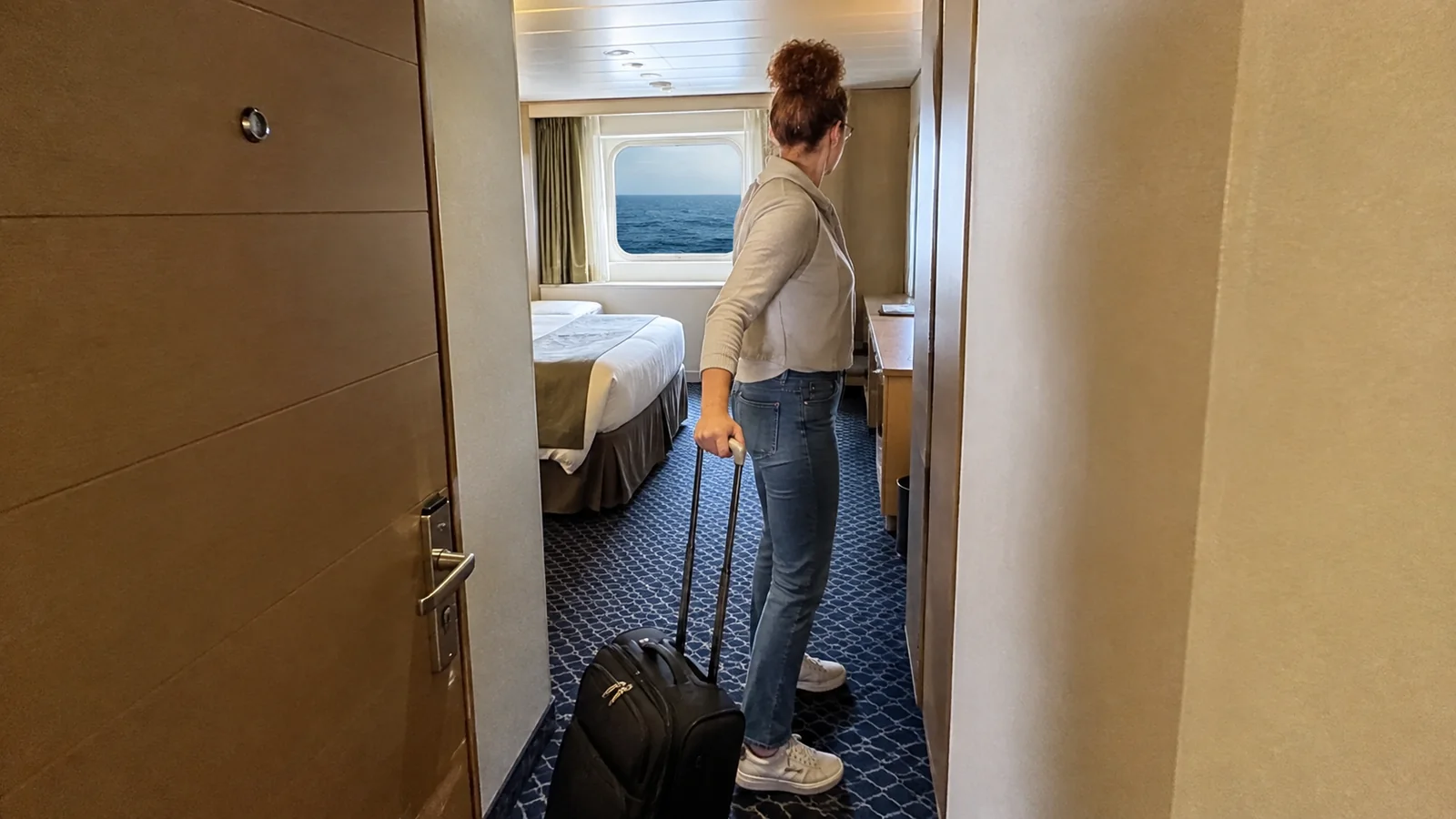 Woman pulls a small suitcase into a ready stateroom.