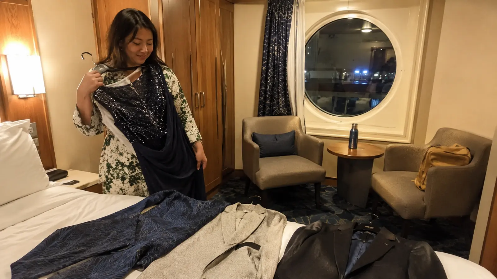 Woman in a floral dress holding a dark shawl over a cruise cabin bed
