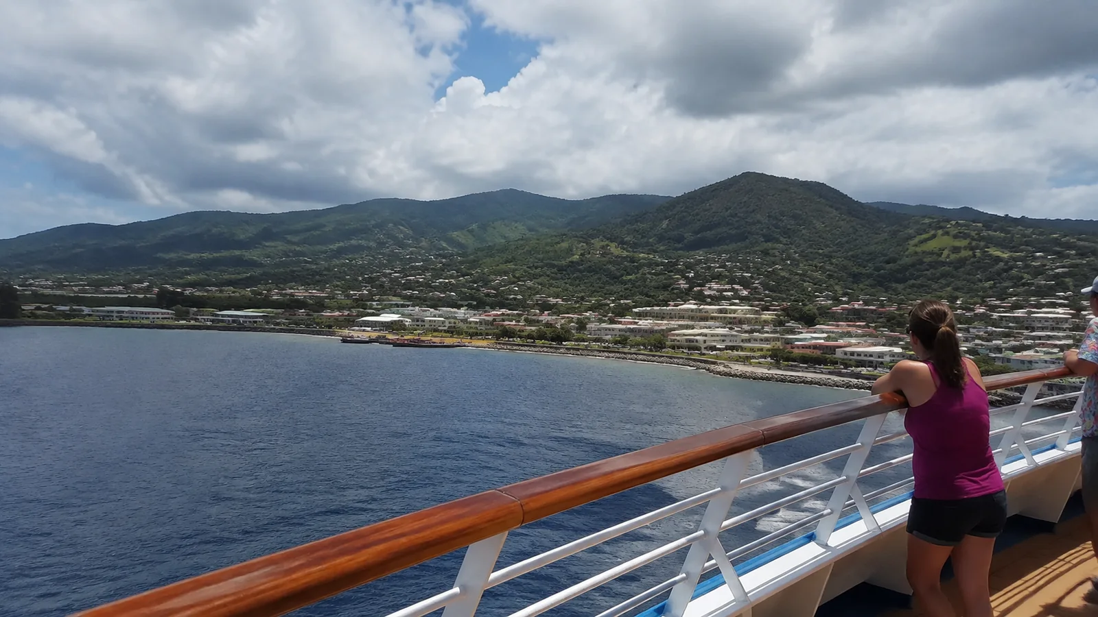 Passenger watching a green island coastline from a cruise railing.