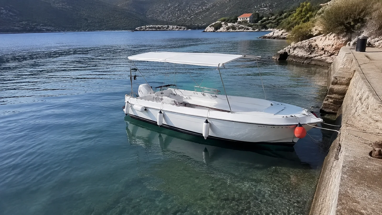 Small covered motorboat floats beside a stone waterfront wall.
