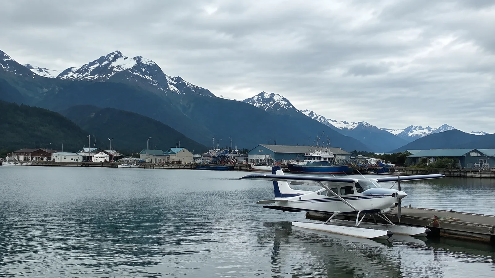 Floatplane is moored in a harbor beneath snowy mountains.