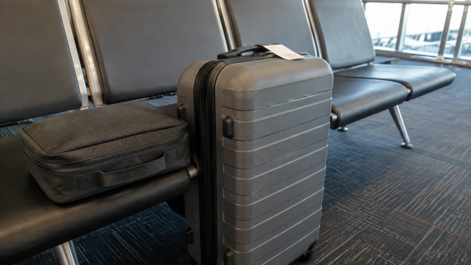 Gray suitcase and a smaller bag rest beside terminal seats.