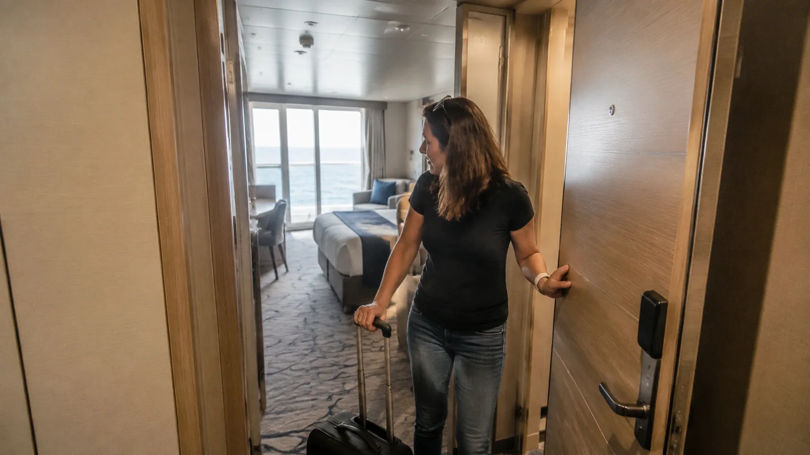 Woman enters a stateroom while pulling a small suitcase.