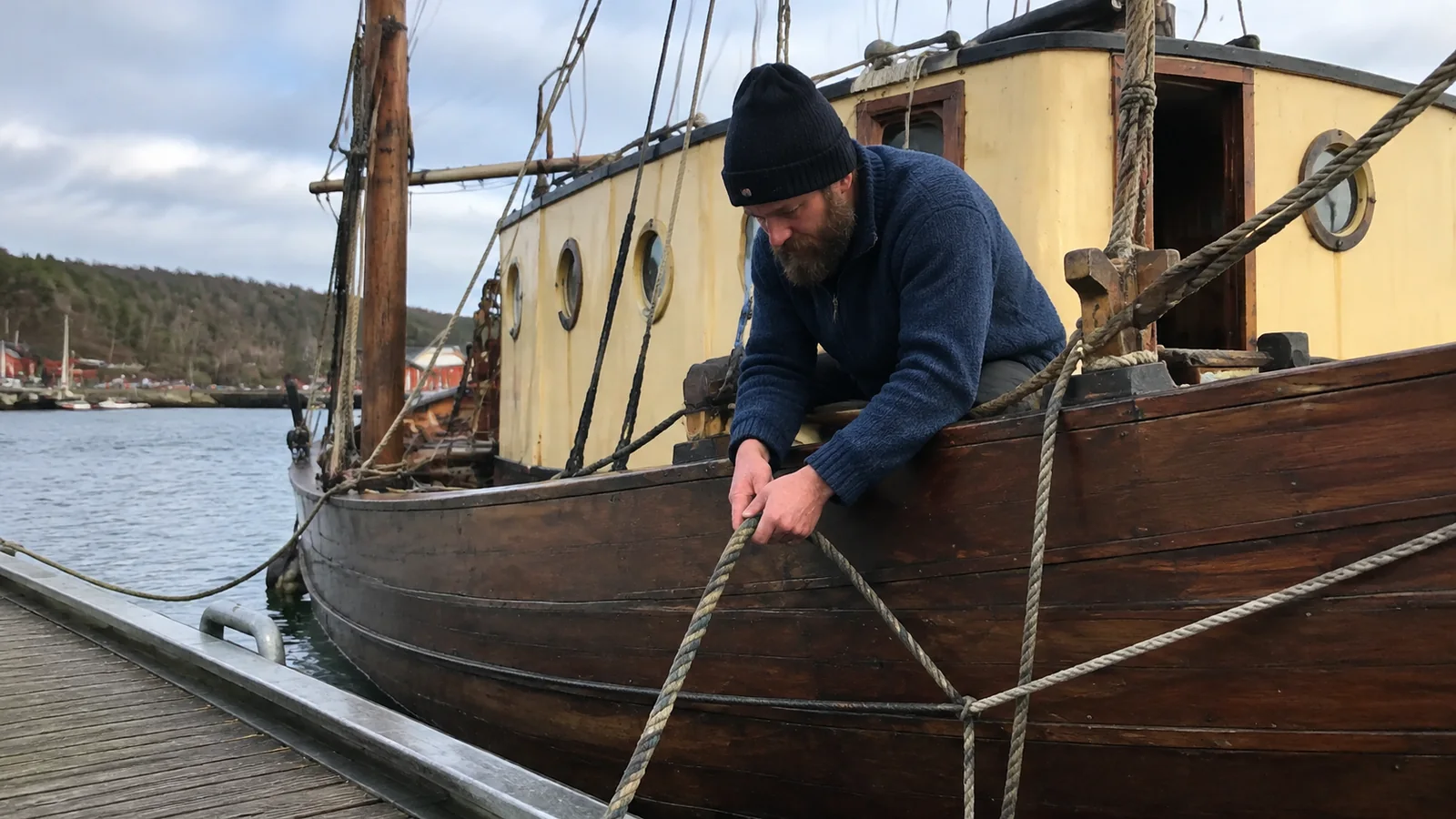 Crew member handling a mooring rope on a wooden boat.
