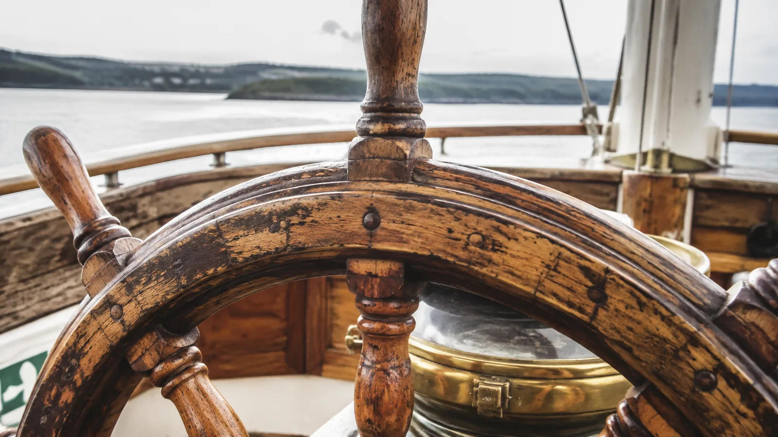 Weathered wooden ship's wheel beside a brass compass housing.