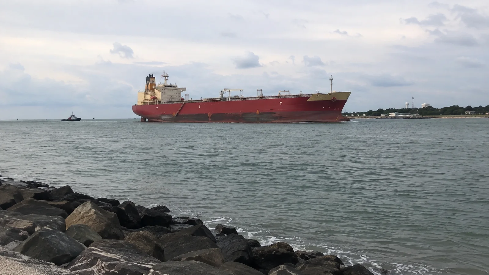 Red-hulled cargo ship moving across a harbor.
