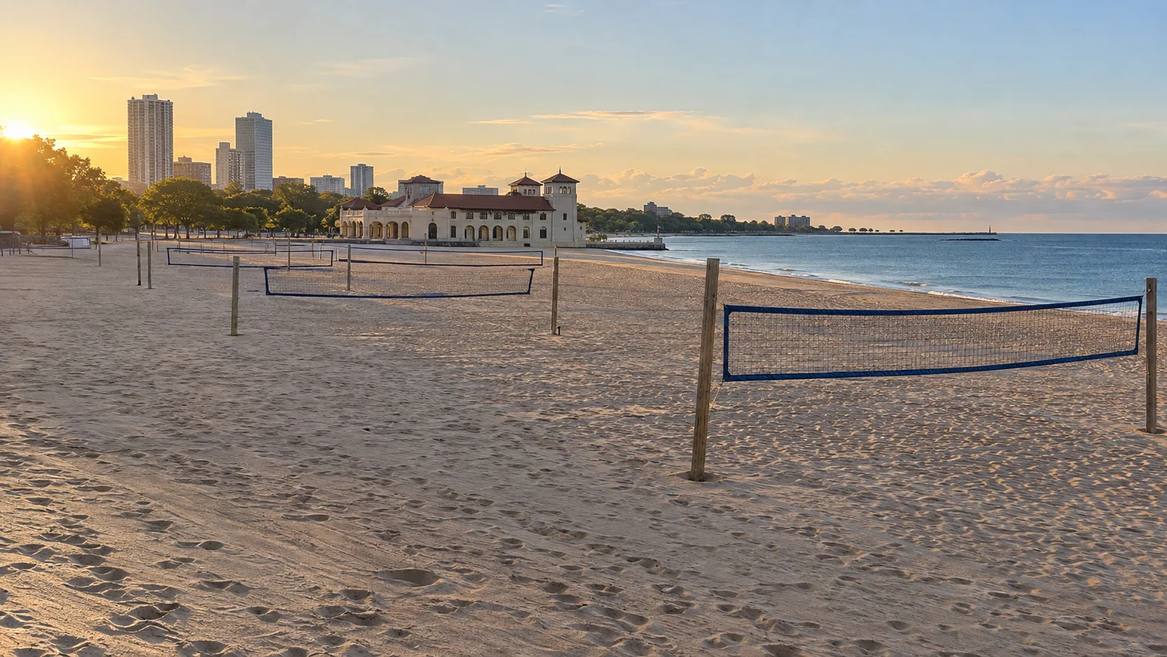 Volleyball nets stretch across Bradford Beach with its historic beach house and Milwaukee skyline at sunrise.
