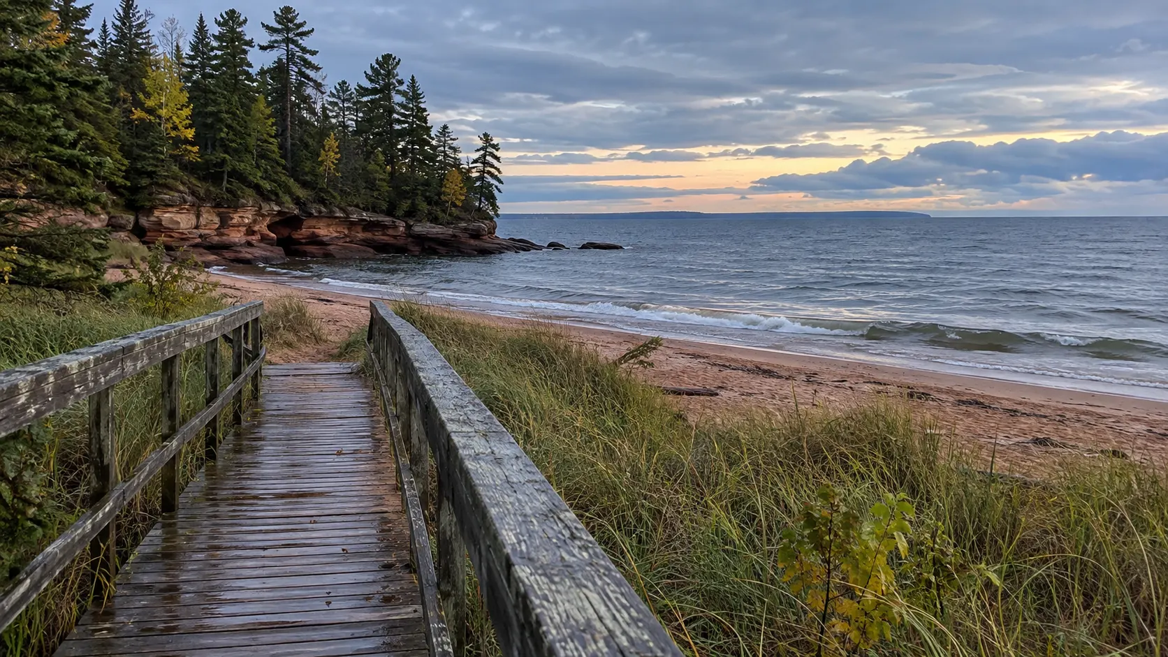 A rain-darkened boardwalk leads to the sandy Lake Superior shore and red sandstone at Big Bay State Park.