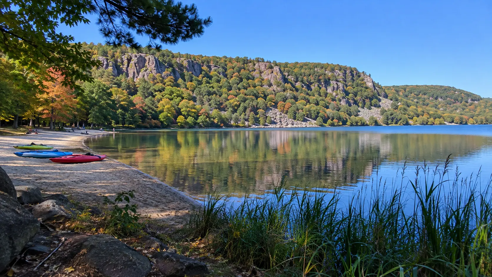 Colorful kayaks rest on a sandy Devil's Lake beach beneath wooded quartzite bluffs in autumn.