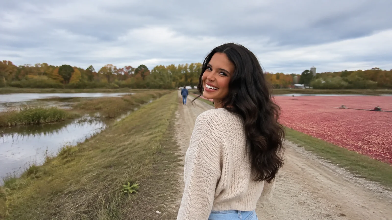 Woman walks along a grassy embankment between cranberry beds.