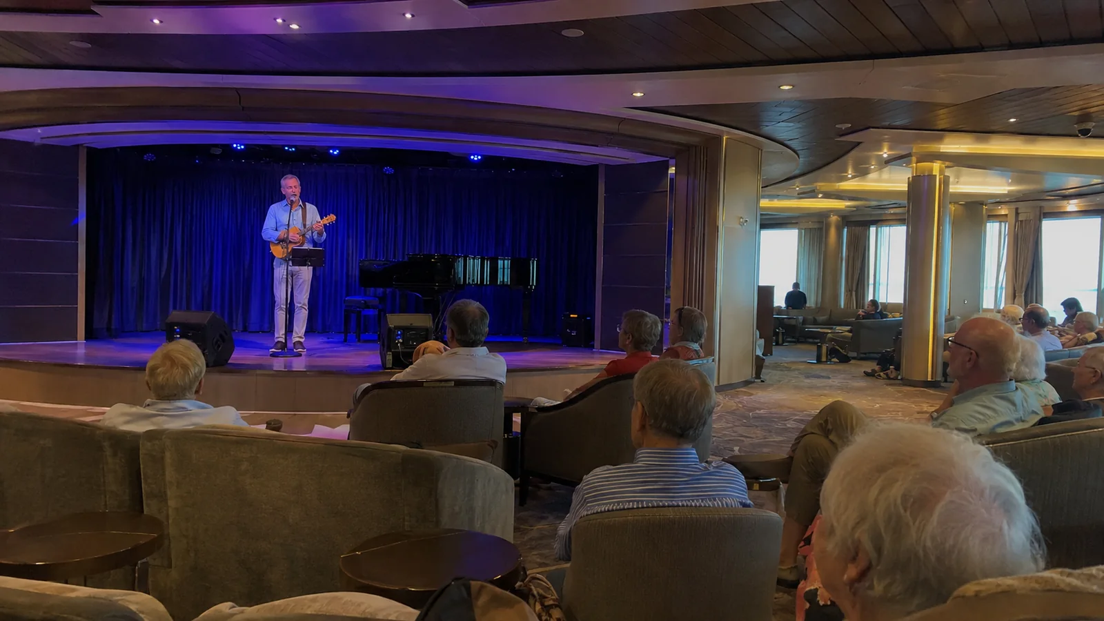 Passengers watching a musician perform in a ship lounge.