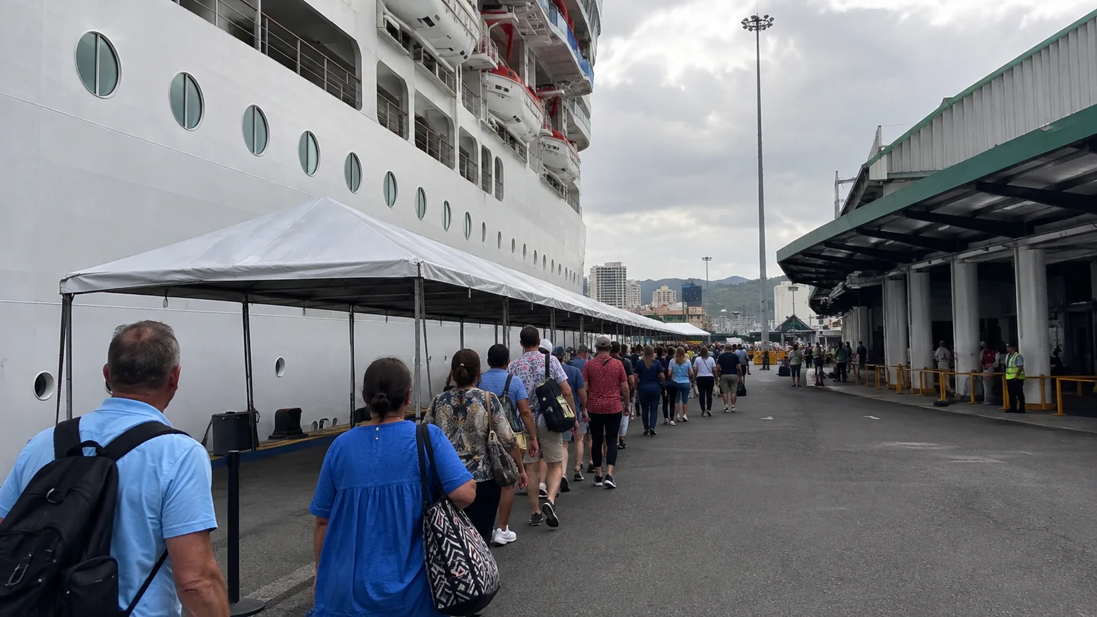 Passengers queuing beside a cruise ship under a long canopy.