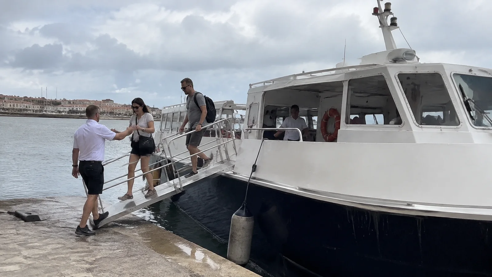 Crew member helping travelers down a small passenger boat's gangway.