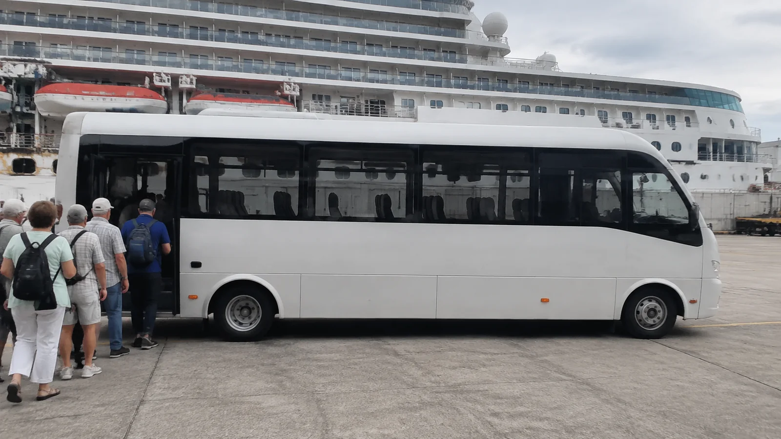 Passengers boarding a shuttle bus beside a docked cruise ship.