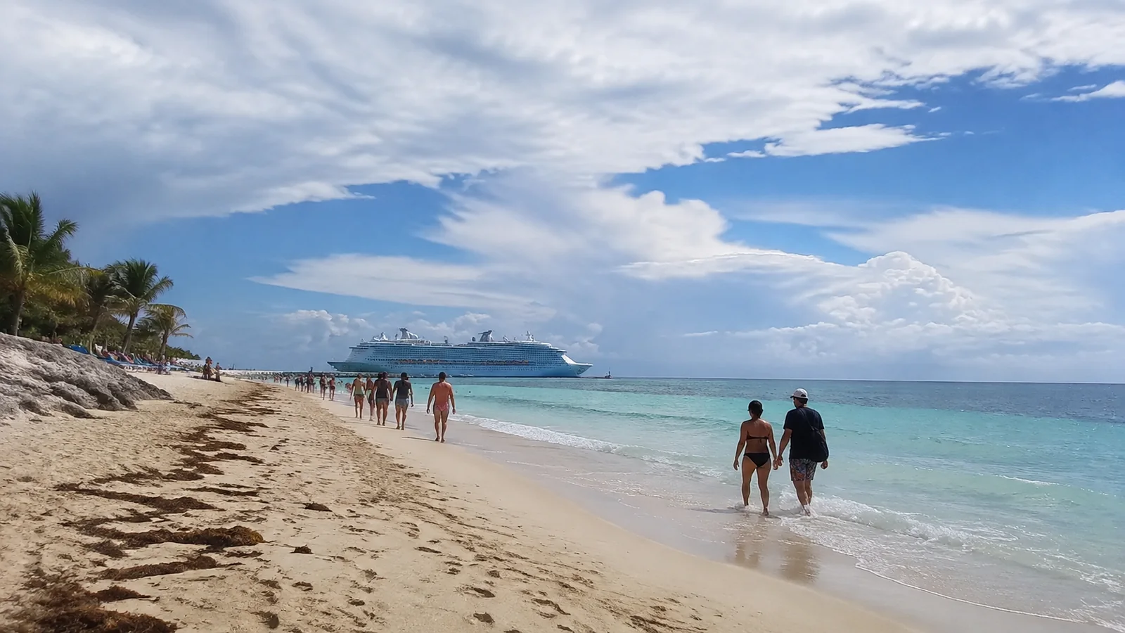 People walking along a white sand beach with a cruise ship offshore